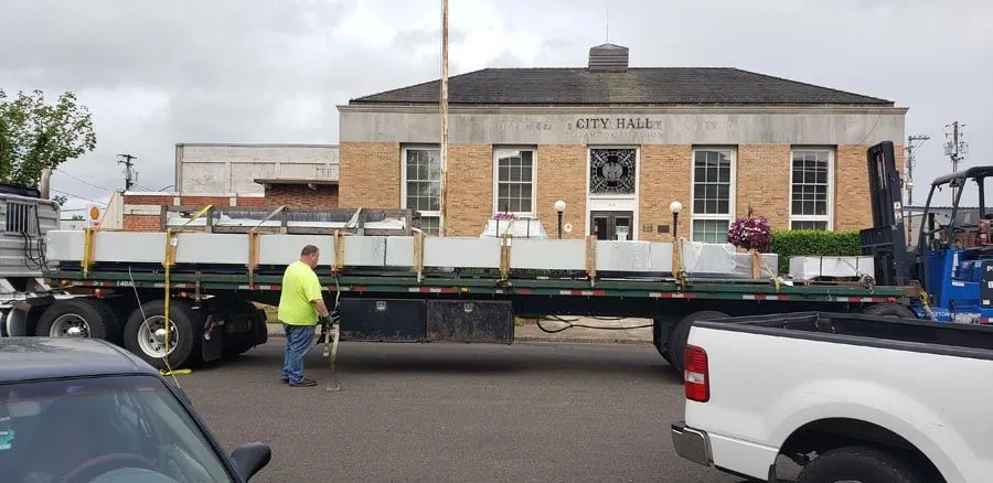 A truck is being loaded with a large piece of metal in front of a building.