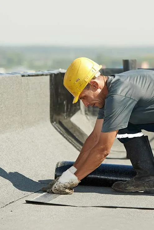 A man wearing a hard hat is working on a roof.