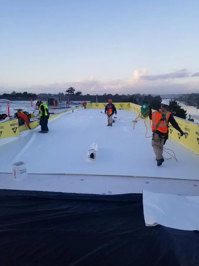 A group of construction workers are working on a white roof.